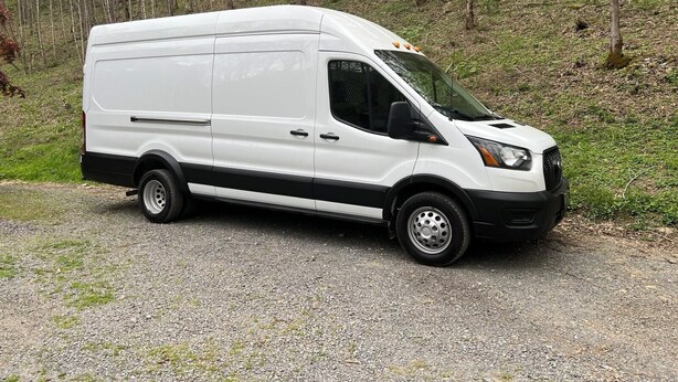 A white van parked on a gravel path in a forested area.