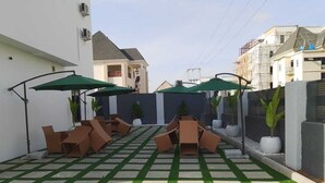 A courtyard with a checkered pattern of artificial grass and stone tiles, surrounded by walls and buildings. - Nook and Cranny Apartment (Abuja)
