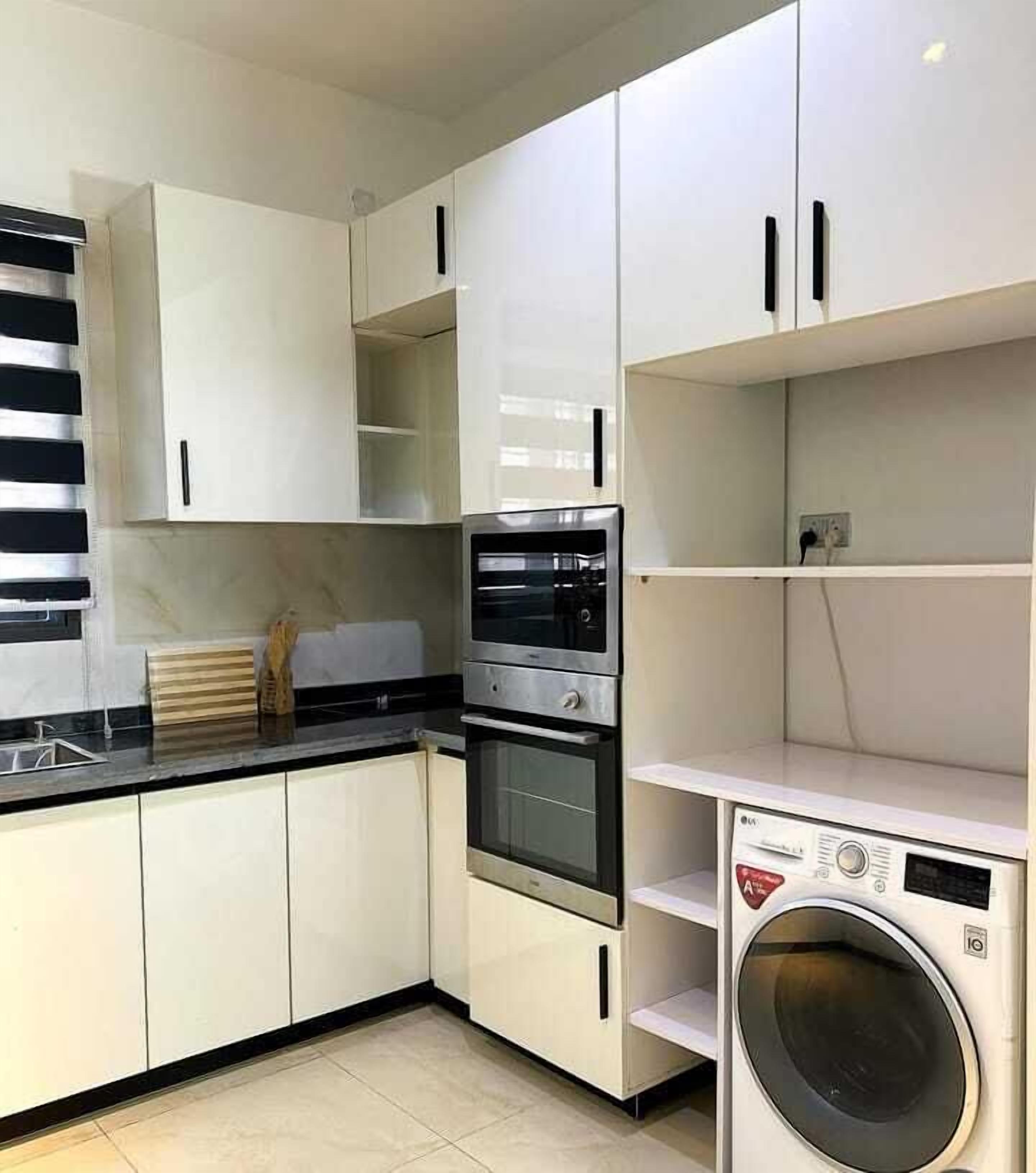 Une cuisine compacte avec des meubles blancs, un four encastré, un four à micro-ondes et un lave-linge.