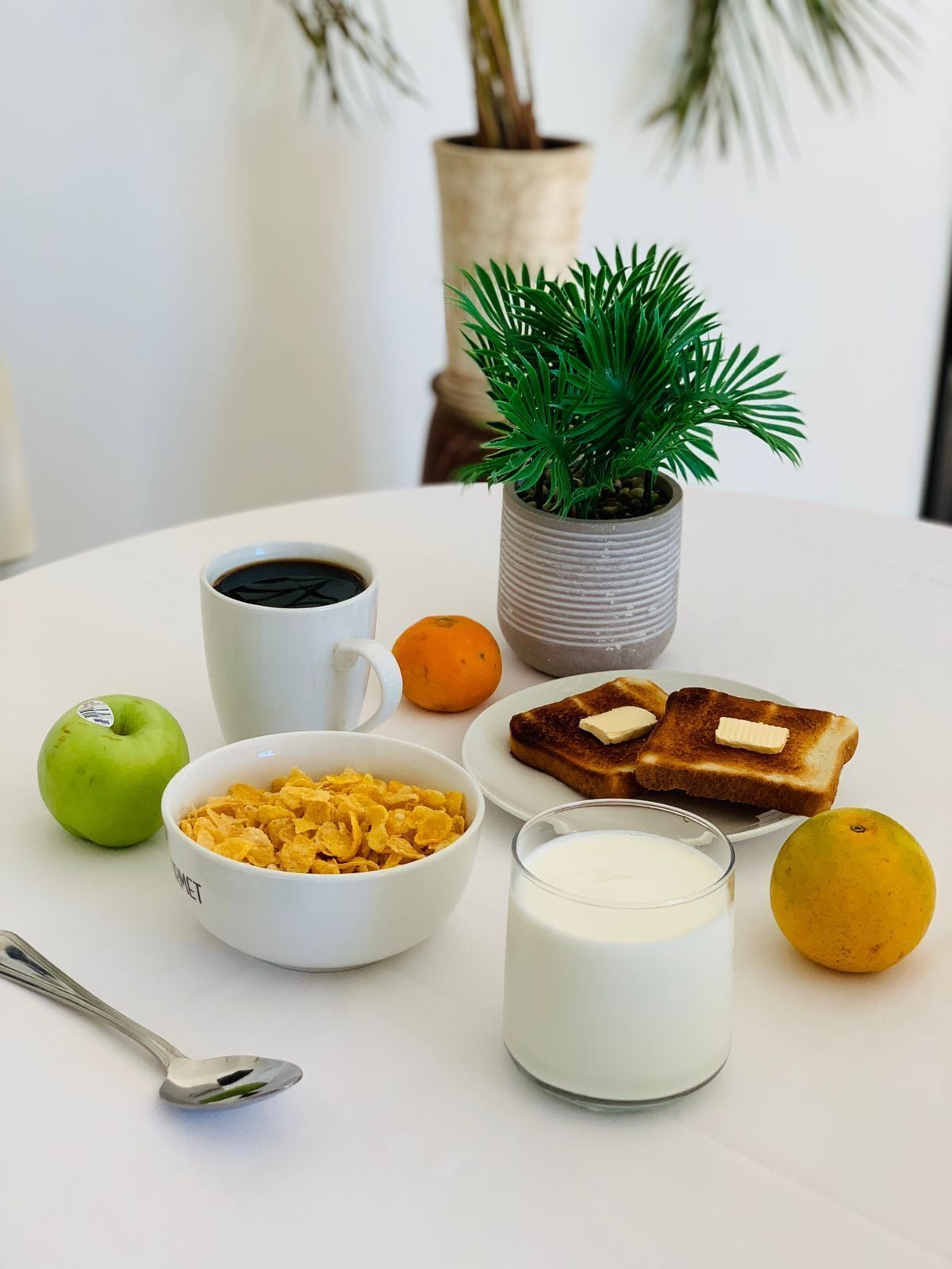 Mesa posta para o café da manhã com cereais, torradas, leite e frutas.