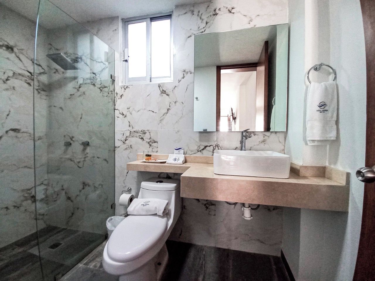 A modern bathroom with a marble floor, a glass shower enclosure, a white toilet, a beige sink, and a mirror above the sink.