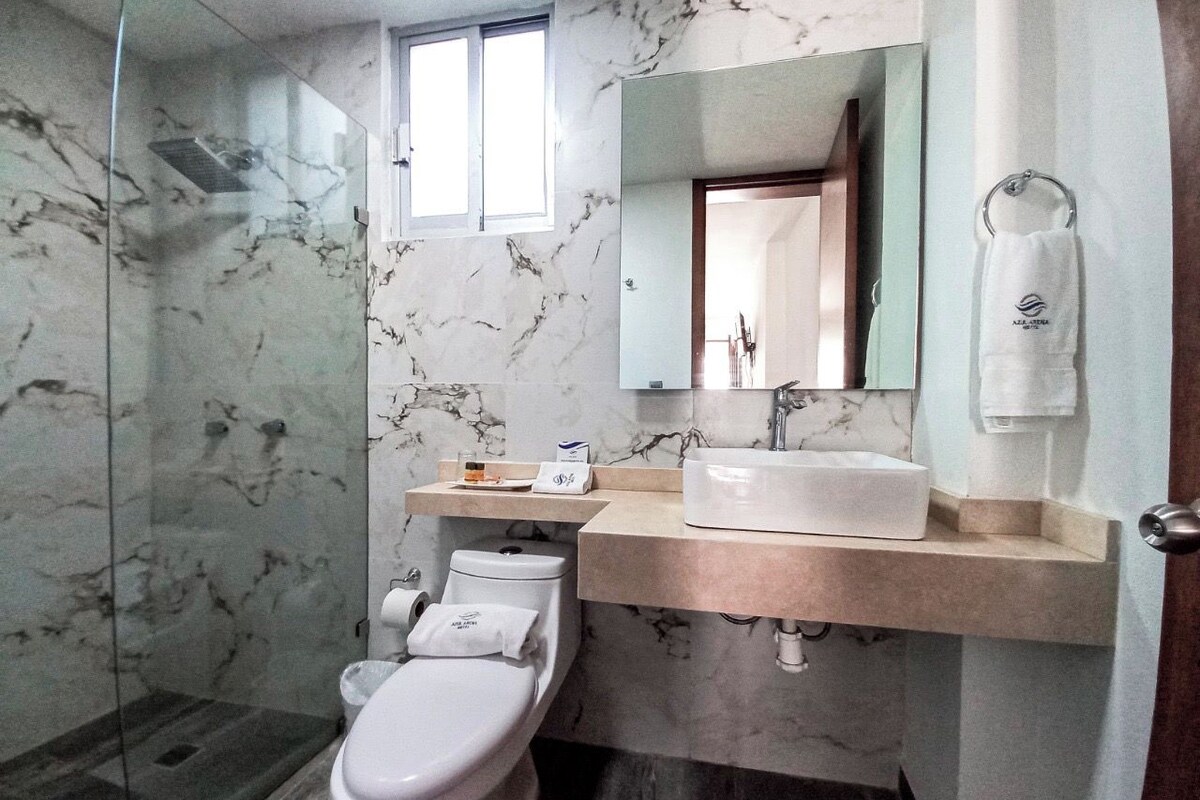 A modern bathroom with a marble floor, a glass shower enclosure, a white toilet, a beige sink, and a mirror above the sink.