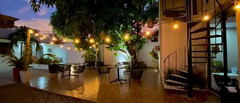 Un patio al aire libre con mesas y sillas, rodeado de macetas y árboles.