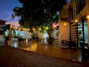 An outdoor patio area with tables and chairs, surrounded by potted plants and trees. - Azul Arena Hotel Boutique (Mazatlan)