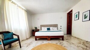 A bedroom with a bed, a chair, a nightstand, and a wall with framed pictures. - Azul Arena Hotel Boutique (Mazatlan)