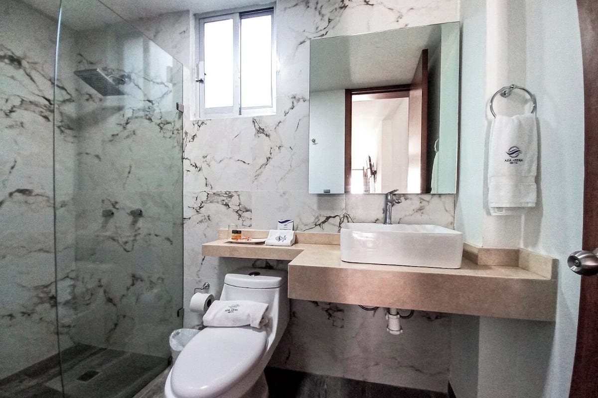 A modern bathroom with a marble floor, a glass shower enclosure, a white toilet, a beige sink, and a mirror above the sink.