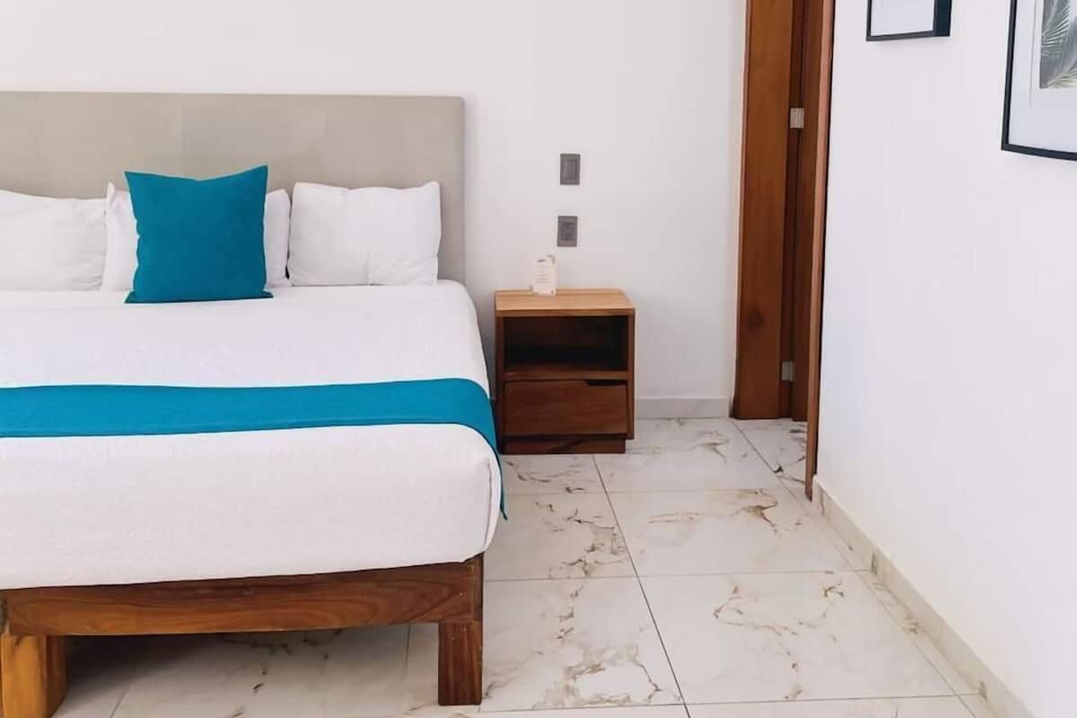 A bedroom with a bed, nightstand, and a door leading to another room.