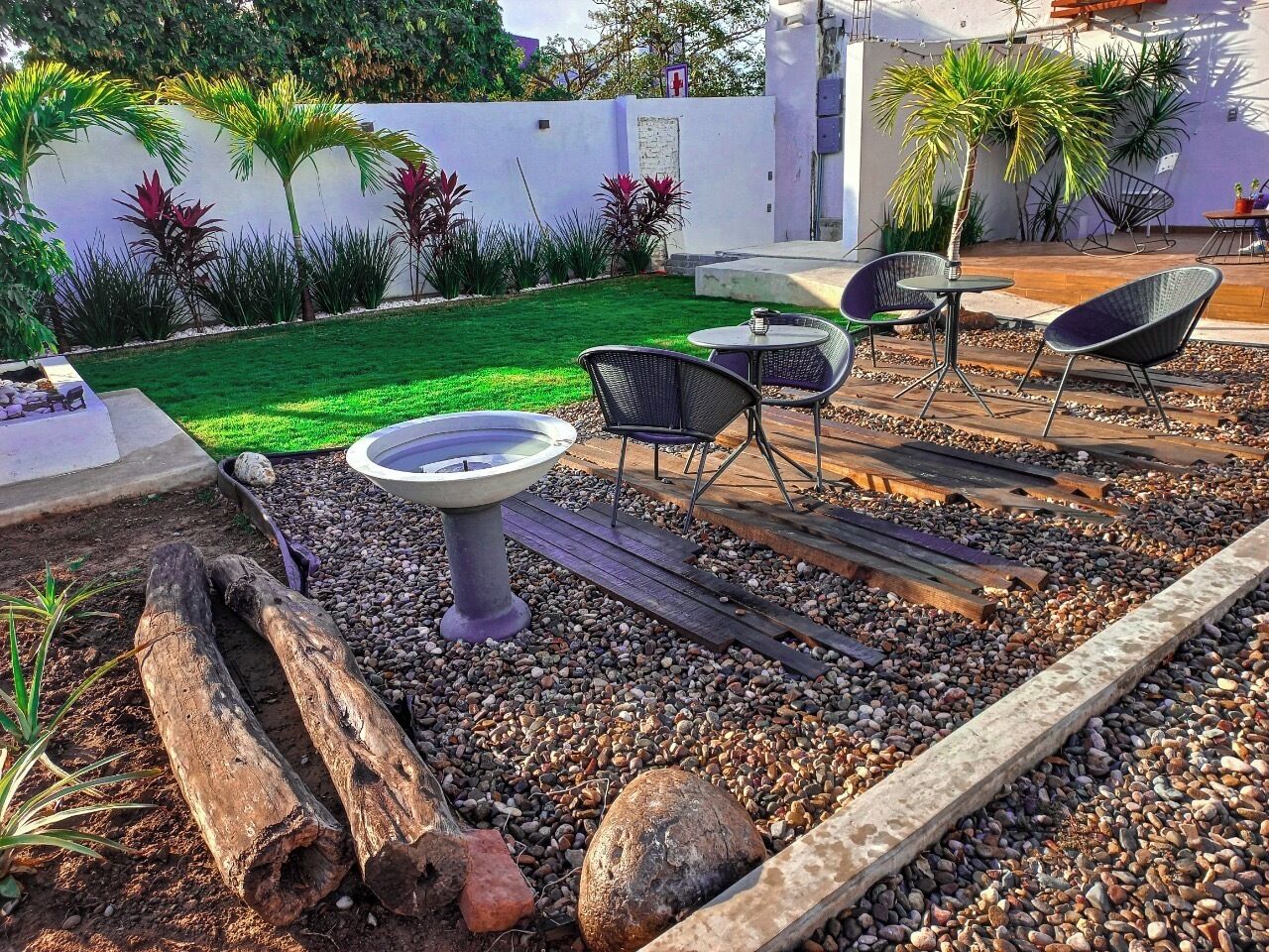 An outdoor patio with a round table, two chairs, a small fountain, and a variety of plants.