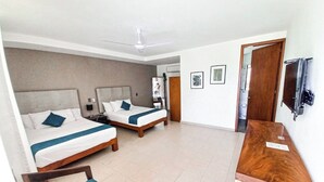 Una habitación de hotel con dos camas, un escritorio de madera, una silla, un ventilador de techo y un televisor.