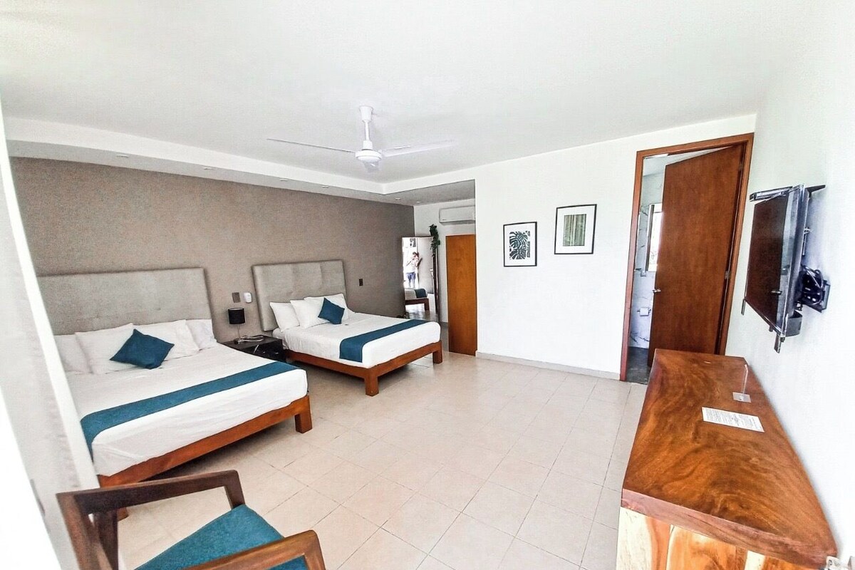 Una habitación de hotel con dos camas, un escritorio de madera, una silla, un ventilador de techo y un televisor.