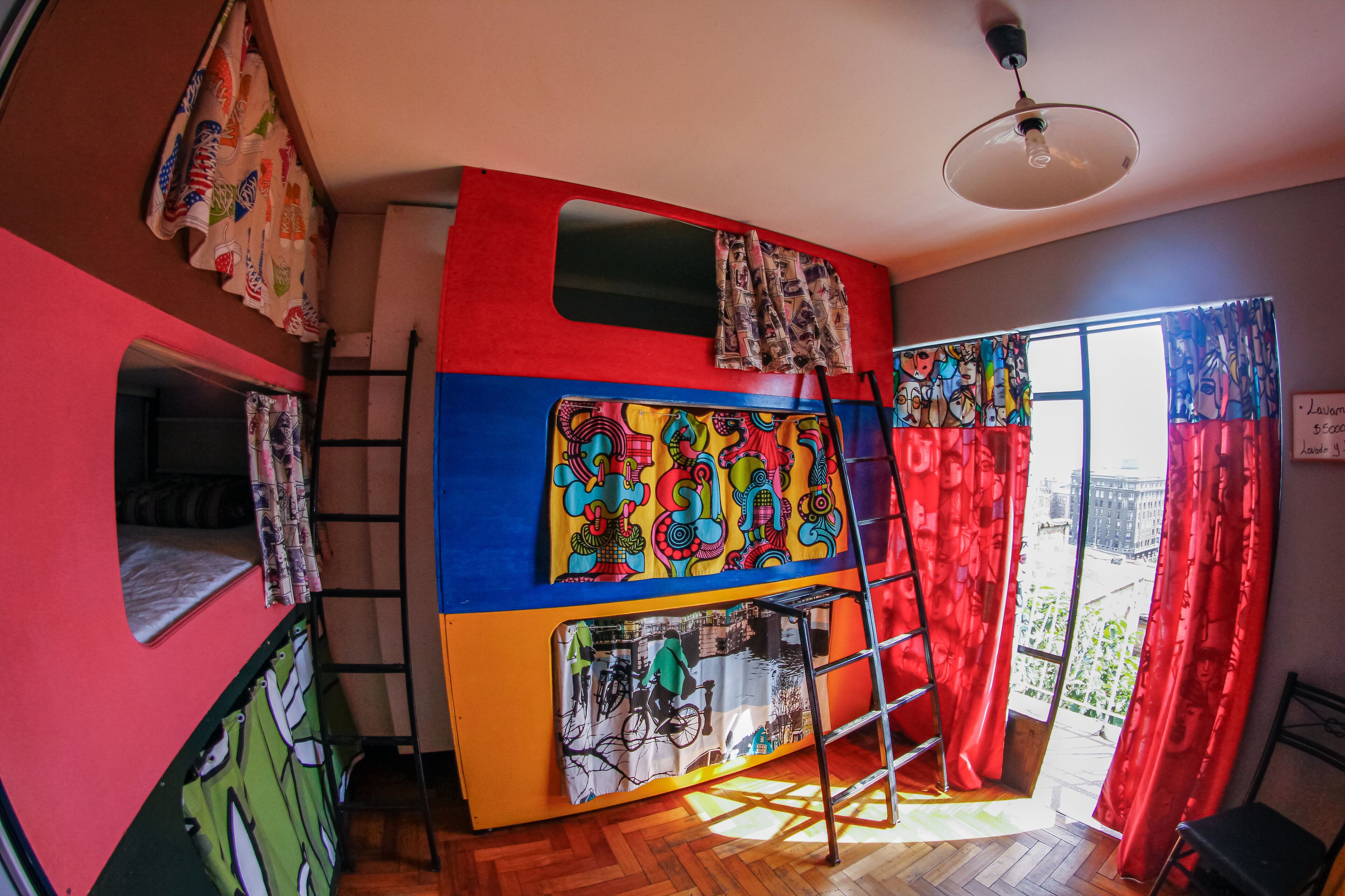 A bunk bed room with a colorful mural, a ladder, and a view of the city through a large window.