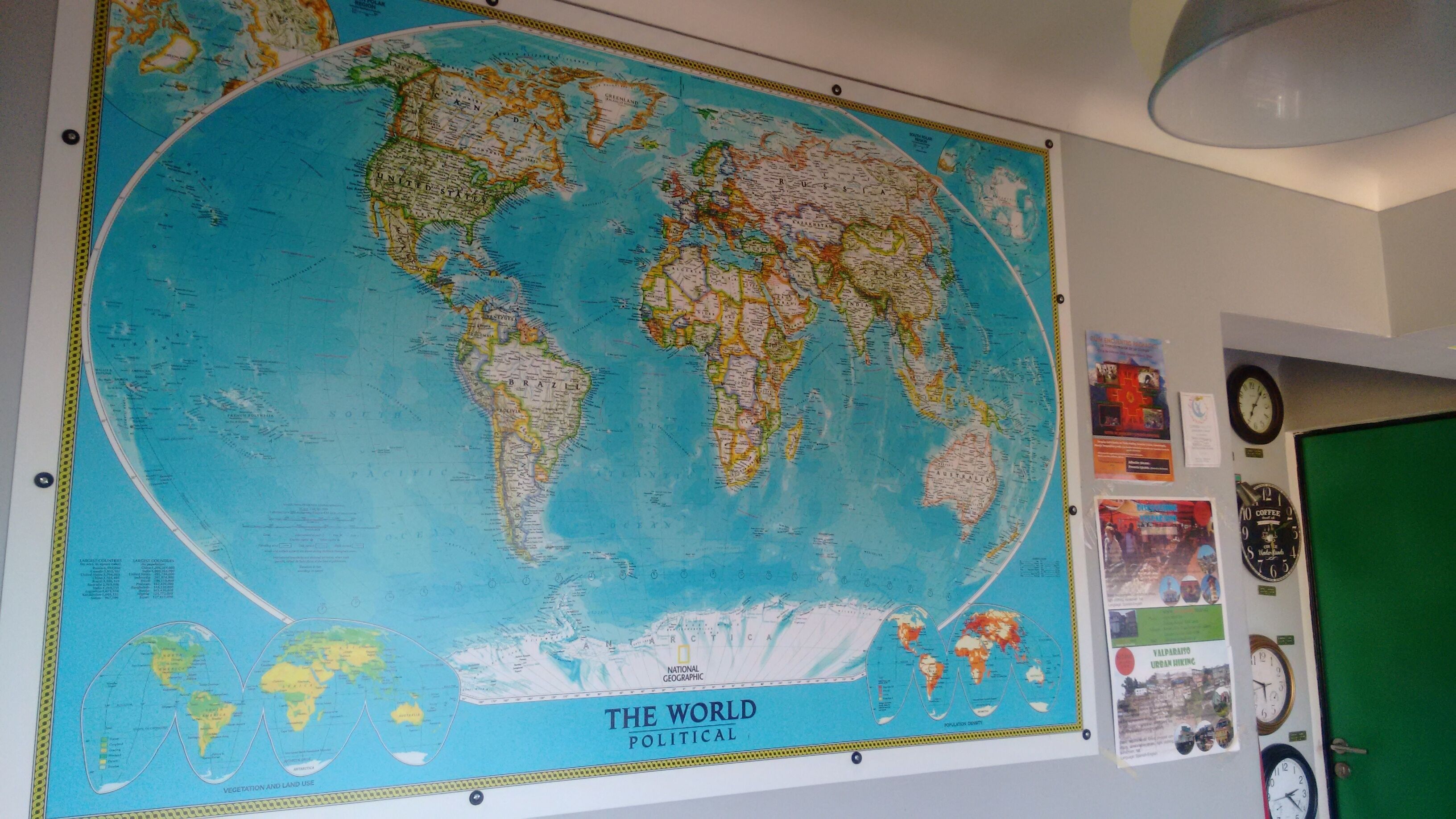Un gran mapa político mundial en una pared, rodeado de relojes y una puerta verde.