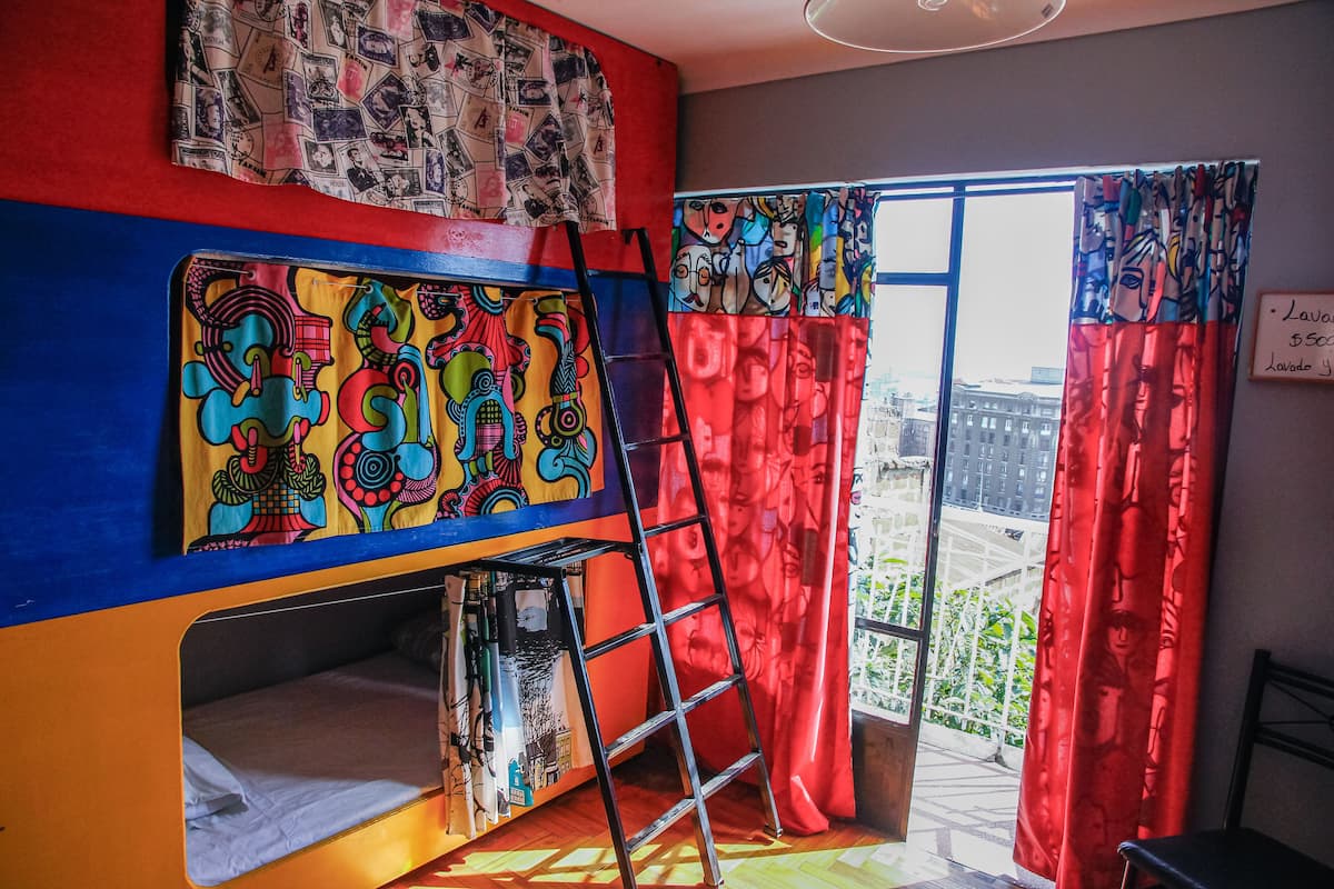 Une chambre avec un lit superposé, des œuvres d’art colorées accrochées aux murs, une échelle et une vue sur la ville grâce à de grandes fenêtres.