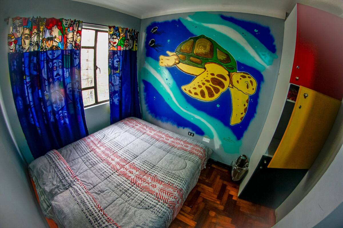 Une chambre à coucher avec un lit, une fenêtre avec des rideaux, une fresque murale représentant une tortue et une armoire.