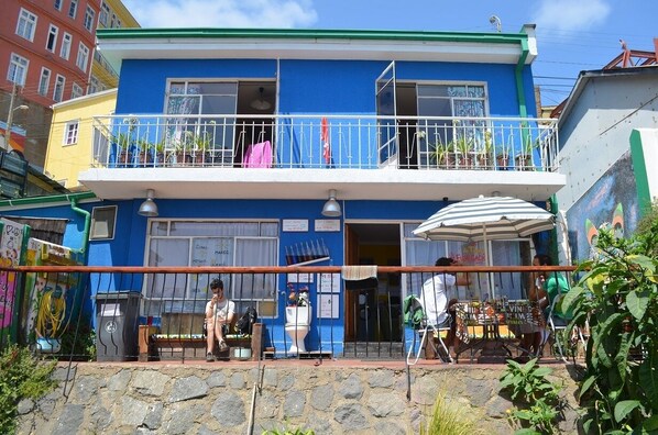 A two-story building with a balcony, a trash bin, and a table with an umbrella. - Hostal La Casa Azul (Valparaíso)