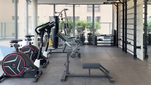 Une salle de sport moderne, équipée de matériel d’exercice, dotée de grandes fenêtres et offrant une vue sur les bâtiments environnants.