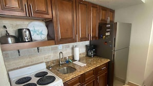 A kitchen with wooden cabinets, a white stove, a stainless steel refrigerator, and a granite countertop. - Sunrise Studio – Balcony with Ocean Views (Daytona Beach Shores)