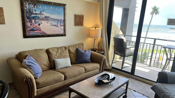 A living room with a sofa, a coffee table, and a view of Waikiki Beach. - Sunrise Studio – Balcony with Ocean Views (Daytona Beach Shores)