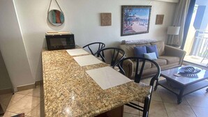 A kitchen with a granite countertop, a microwave, a trash can, and a dining area with a sofa and chairs. - Sunrise Studio – Balcony with Ocean Views (Daytona Beach Shores)
