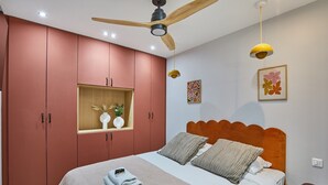Un dormitorio con cama, ventilador de techo, estante con adornos y una obra de arte en la pared.