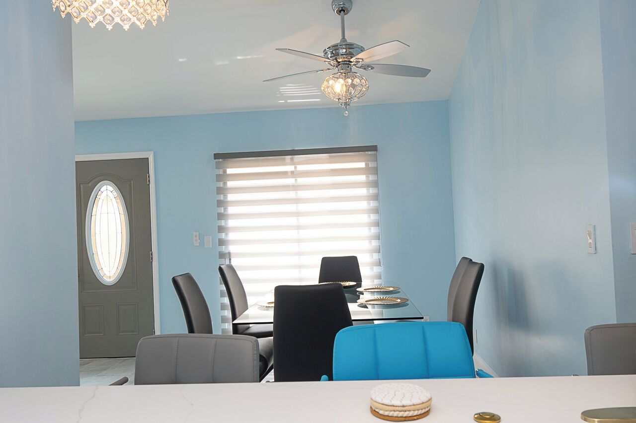 Comedor con una mesa lista para cuatro personas, ventilador de techo y ventana con persianas.