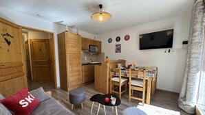 Un salon chaleureux avec un canapé, une petite table et une table à manger en bois, ainsi que des chaises. Il y a également un coin cuisine avec des placards en bois et un téléviseur fixé au mur.