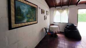 Una habitación con un cuadro grande enmarcado, una mesita con una silla, y un sillón de peluche.