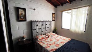 Un dormitorio con una cama, cabecera, mesita de noche, planta en maceta y dos cuadros en la pared.