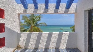 Un balcon avec vue sur l’océan, les palmiers et un ciel dégagé.