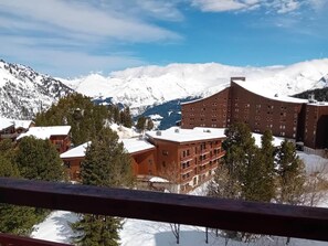 Estância de montanha coberta por neve, com vários edifícios, incluindo uma construção destacada com telhado vermelho e um grande edifício de tijolos com varandas.