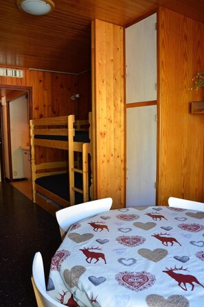 Ein Zimmer mit einem Etagenbett, einem runden Tisch mit gemustertem Tischläufer und Holzwänden.