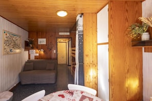 Ein gemütliches Zimmer mit Holzbalkendecke, einer Couch, einem Tisch mit gemustertem Tuch und einer Tür zu einem weiteren Raum.
