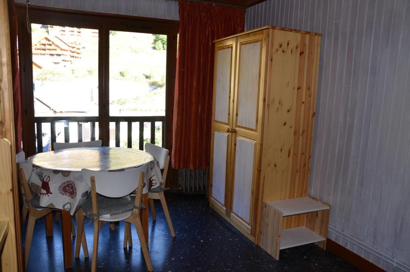 A room with a round table, four chairs, a wooden cabinet, and a view through a door.