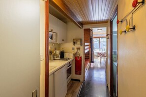 A narrow hallway leading to a kitchen with basic appliances and a dining area visible through an open door.