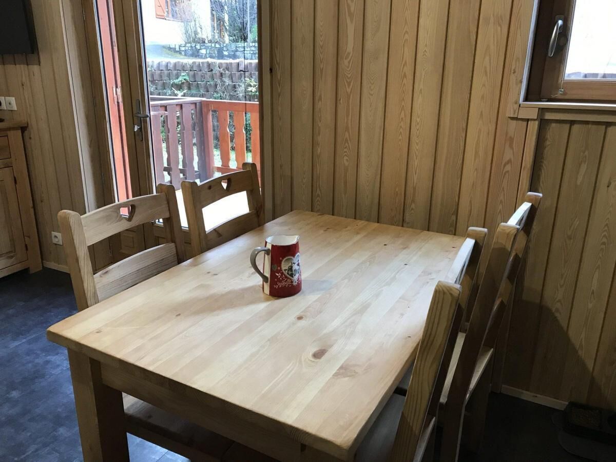 A wooden dining table with four chairs, a red mug, and a view of a wooden deck outside.
