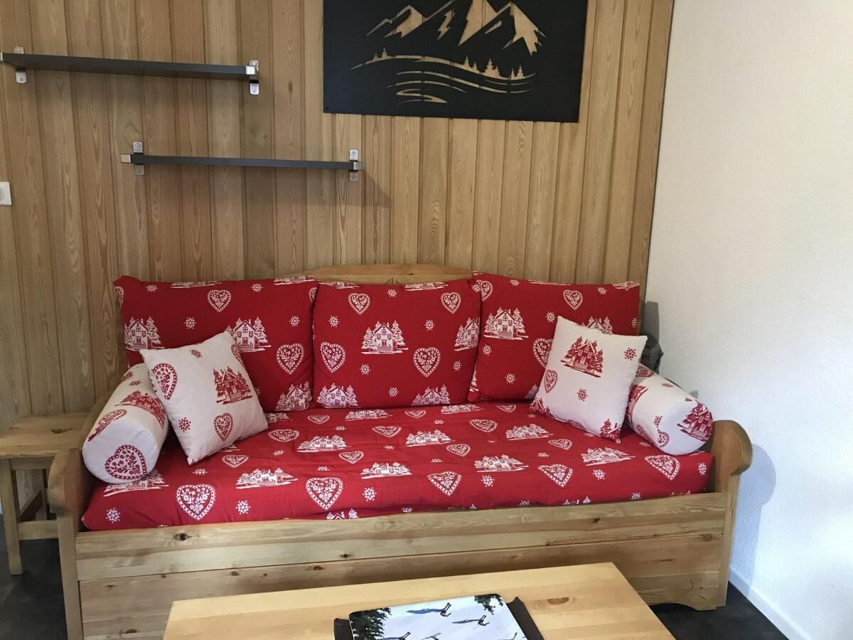 Un canapé en bois avec des coussins à motifs rouges et blancs, une table basse en bois et un mur en bois orné d’un tableau encadré de noir.