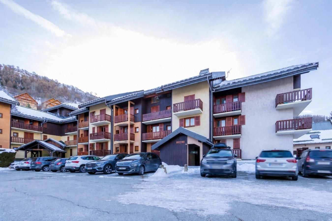 Ein mehrstöckiges Hotel mit Balkonen, einem Parkplatz und einer Bergkulisse.
