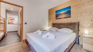 Een slaapkamer met een houten hoofdbord, een bed met witte lakens en handdoeken, een schilderij van een berglandschap, en een houten vloer.
