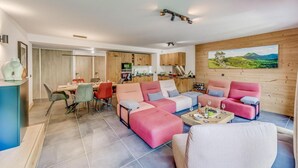 Een moderne woonkamer met een roze zithoek, een eethoek met een houten tafel en stoelen, en een keuken met houten kastjes.