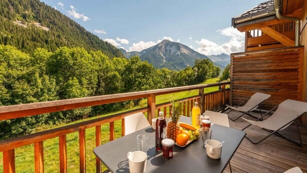 Een houten terras met een gedekte tafel voor twee, met uitzicht op een bergachtig landschap.