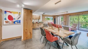 Een moderne keuken met houten kastjes, een eethoek met tafel en stoelen, en een balkon met uitzicht op groen.