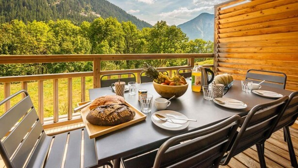 A wooden deck with a table set for dining, overlooking a mountainous landscape.