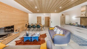 A modern living room with a wooden ceiling, a sofa, a dining table with chairs, and a kitchen area.