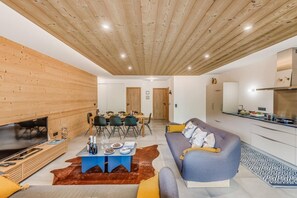 Ein modernes Wohnzimmer mit Holzbalkendecke, einer Couch, einem Esstisch mit Stühlen und einer Küchenzeile.