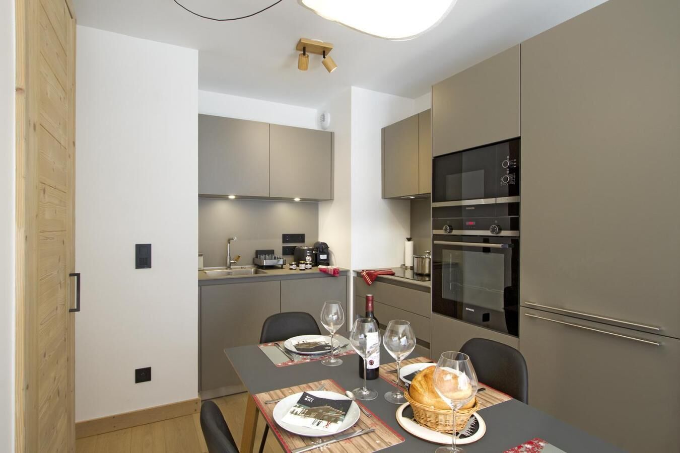 Une cuisine compacte dotée d’appareils électroménagers modernes, un coin repas avec une table dressée pour deux personnes et un petit espace salon.