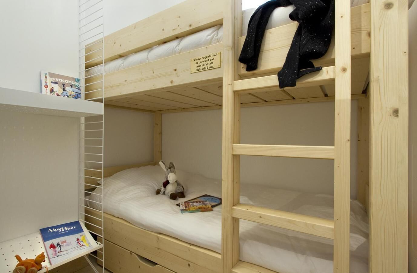 A bunk bed room with a small shelf holding a book and a plush toy.