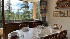 Mesa de comedor dispuesta para seis personas, con vista a árboles y montañas a través de una ventana.