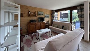 Una sala de estar con un sofá, una mesa de centro y un televisor. Hay una pared de madera con cuadros y una ventana con cortinas.
