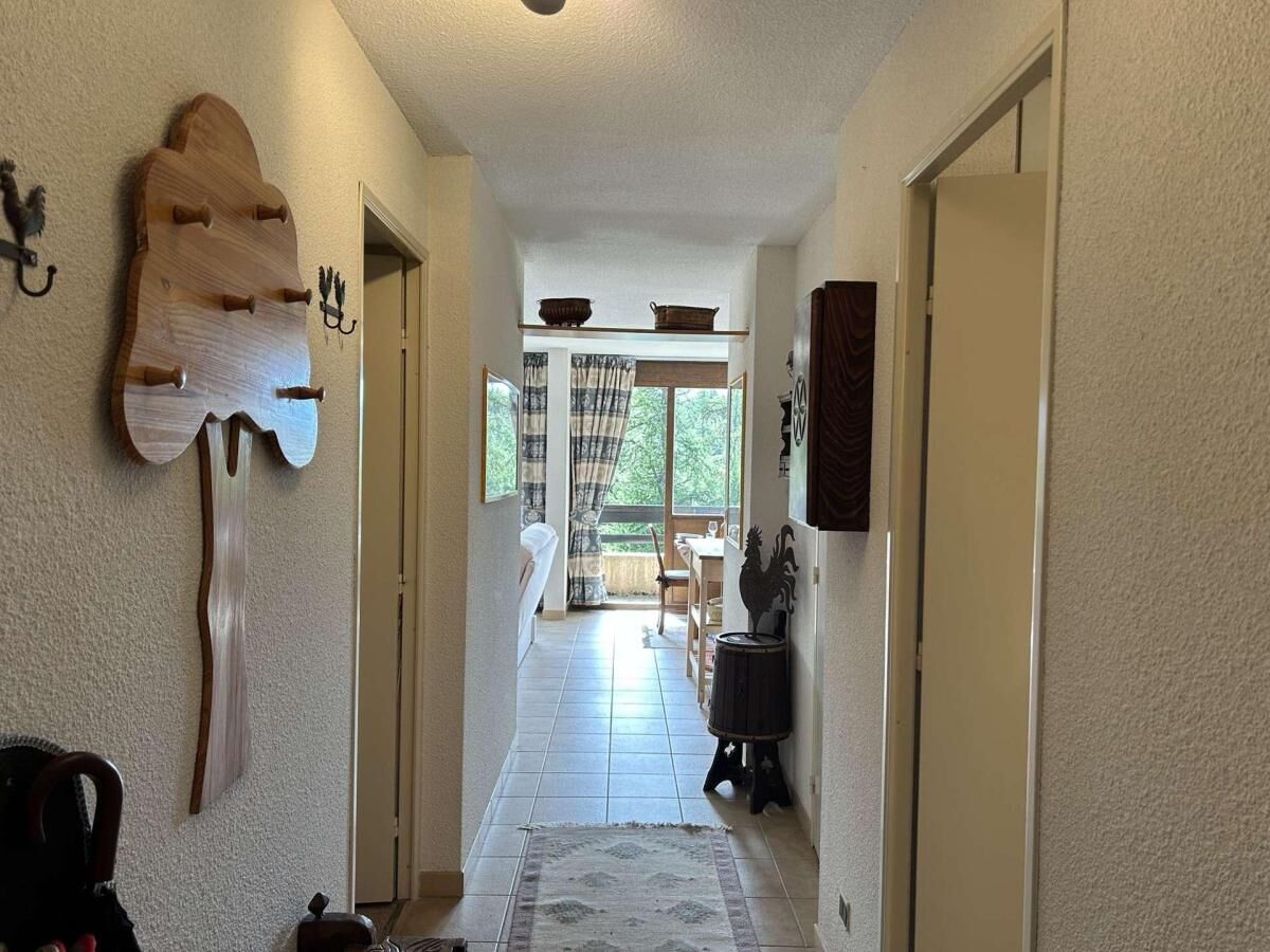 Un pasillo con un adorno de pared de madera, una alfombra y una puerta que da a un comedor con vistas al exterior.