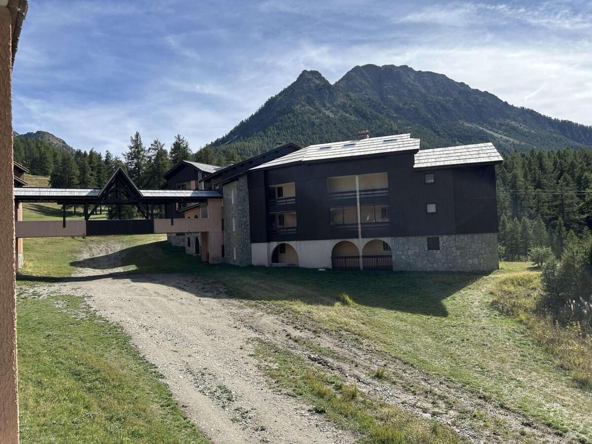 Un edificio moderno con fachada de piedra y varios balcones, rodeado de un paisaje montañoso.